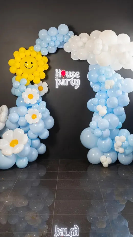A pastel balloon arch with a smiling sun and a House of Party sign